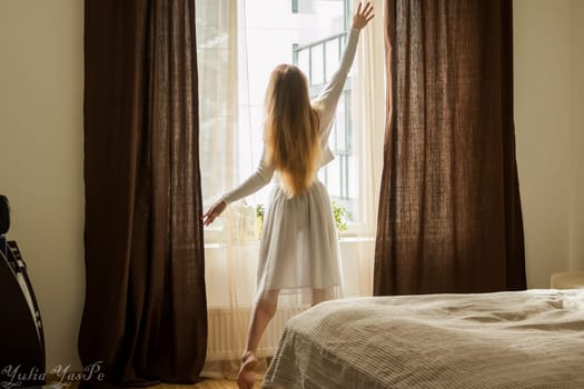 Hand Opens Curtain on the Wooden Cottage House Window. Bright Sunlight Shines Through. Beautiful snowy Winter morning light behind the Chalet Window.