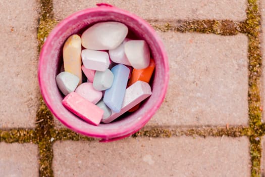 A bucket of colorful chalk on the asphalt in plastic box. Drawing with chalk on the pavement. crayons for drawing.