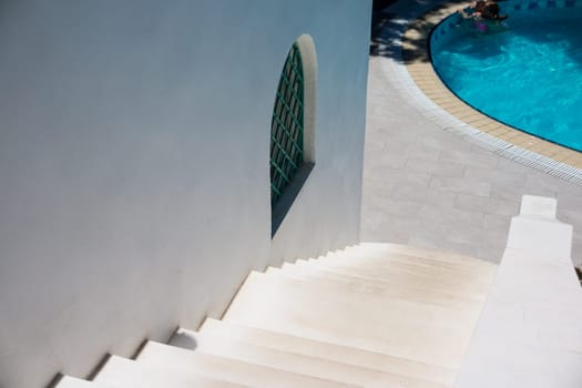white stone stairs, ladder outside on sunny day. white house with swimming pool.
