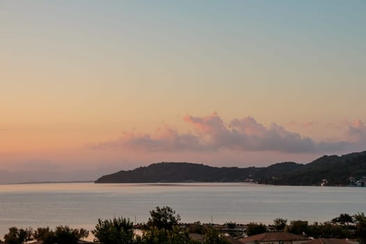 Colorful vanilla sky under calm silver sea and rocky mountains at dawn