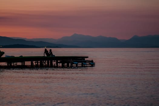 Sunset time on river. Orange sunset landscape with pier and men. Vivid orange sky view. Romantic evening sunset in tropics.