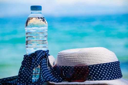 Vacation concept. Essentials on the sea beach. Bottle of drinking water, sunglasses, hat, flip-flops.