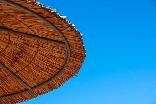 Straw roof of sun umbrella against the blue sky. Vacation topic.