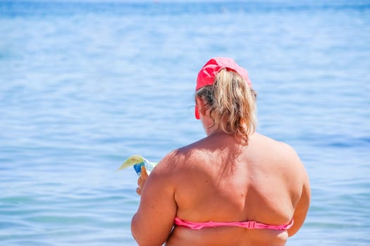 mature woman in swimwear at the sea. Overweight woman in swimsuit comes in water in time of surf, rear view