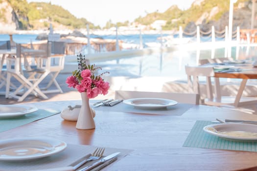 Summer terrace of the restaurant. On the tables laying with white plates of wine glasses and white vases with the colors of the bride. In the background, waiters