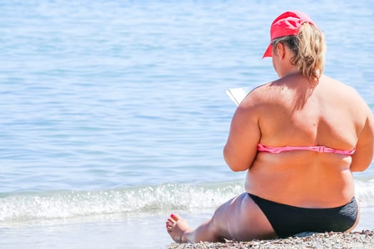A woman wearing a hat, sitting on the beach staring at the sea