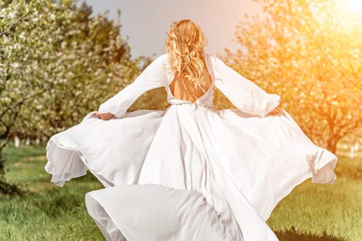 Woman white dress park. A woman in a white dress runs through a blossoming cherry orchard. The long dress flies to the sides, the bride runs rejoicing in life