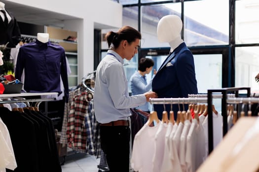 Asian worker looking at hangers with casual wear, arranging fashionable clothes before store opening. Employee wearing formal shirt, working with trendy merchandise in modern boutique. Fashion concept