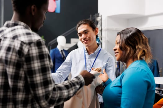 Stylish couple looking at elegant shirt, asking store employee about price in modern boutique. Shopaholic african american woman shopping for casual wear, buying clothes for new wardobe