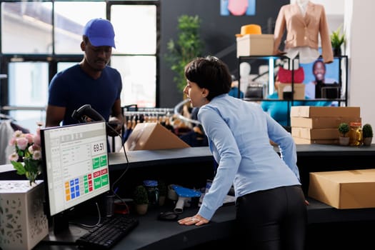 Caucasian worker discussing with courier, preparing packages for shipping in modern boutique. Employee standing at counter desk, checking logistics report on tablet computer. Fashion concept