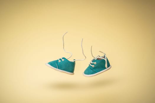 Flying baby shoes with flying laces on yellow background. Newborn baby concept with levitation