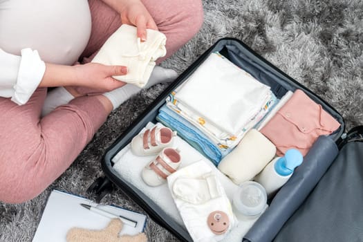 Pregnant woman packing baby clothing in suitcase