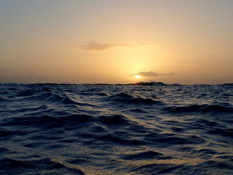 A fiery sunset paints the sky and the ocean with warm colors as seen from the waters of Waikiki beach on Oahu, Hawaii. Clouds add texture and depth to the scenic view.