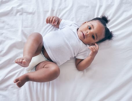 Baby, portrait and girl on a bedroom bed feeling relax and calm in a nursery after rest. Young newborn, child and kid with a diaper in the morning with wellbeing and childcare from above in a house.