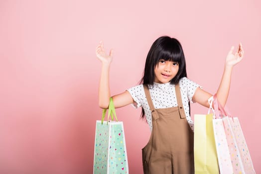 Asian little kid 10 years old smiling holding multicolor shopping bags in hands at studio shot isolated on pink background, Portrait of Happy child girl shopper lifestyle, Black friday concept