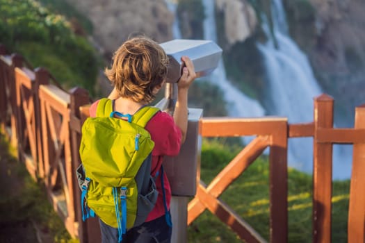 Boy tourist with a backpack on the background of Duden waterfall in Antalya. Famous places of Turkey. Lower Duden Falls drop off a rocky cliff falling from about 40 m into the Mediterranean Sea in amazing water clouds. Tourism and travel destination photo in Antalya, Turkey. Turkiye.