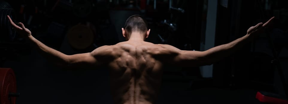 Back view of shirtless man with sculpted body in gym