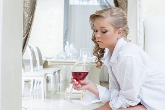 Beautiful young girl thoughtfully looks at glass of wine, close-up