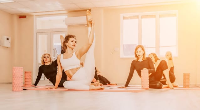 Group of young womans fitness instructor in Sportswear Leggings and Tops, stretching in the gym before pilates, on a yoga mat near the large window on a sunny day, female fitness yoga routine concept.