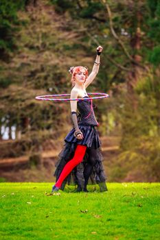 Young beautiful woman in circus costume play with hula hoop in the park.