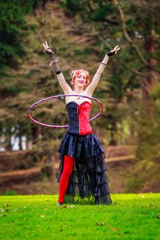 Young beautiful woman in circus costume play with hula hoop in the park.