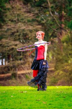 Young beautiful woman in circus costume play with hula hoop in the park.