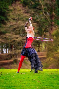 Young beautiful woman in circus costume play with hula hoop in the park.