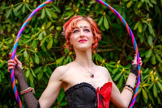 Young beautiful woman in circus costume play with hula hoop in the park.