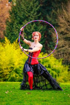 Young beautiful woman in circus costume play with hula hoop in the park.