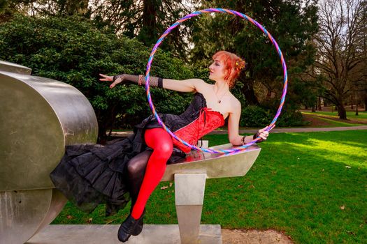 Young beautiful woman in circus costume play with hula hoop in the park.