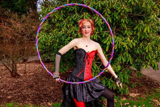 Young beautiful woman in circus costume play with hula hoop in the park.