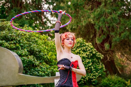 Young beautiful woman in circus costume play with hula hoop in the park.