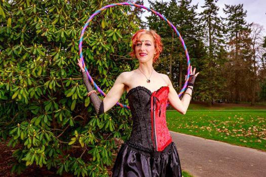 Young beautiful woman in circus costume play with hula hoop in the park.