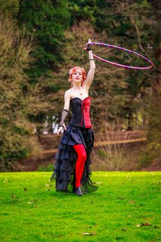 Young beautiful woman in circus costume play with hula hoop in the park.