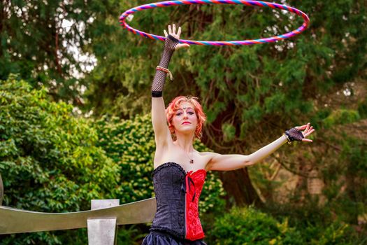 Young beautiful woman in circus costume play with hula hoop in the park.