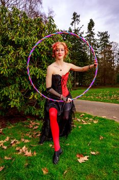 Young beautiful woman in circus costume play with hula hoop in the park.