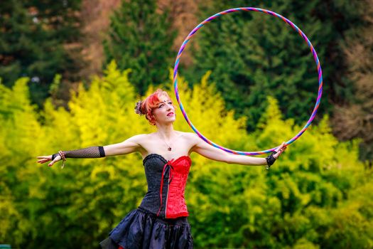 Young beautiful woman in circus costume play with hula hoop in the park.