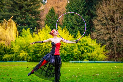 Young beautiful woman in circus costume play with hula hoop in the park.