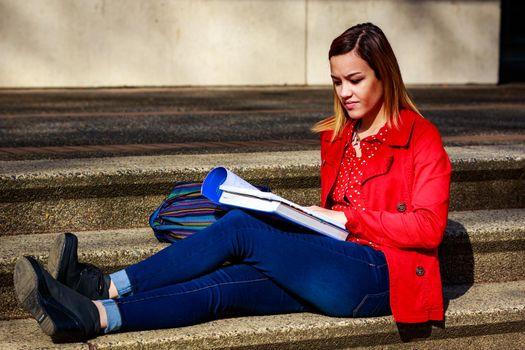 A young female college student study books outside of library.