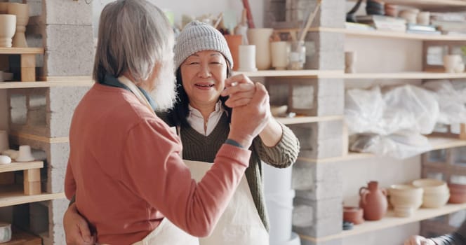 Pottery, creative and senior couple talking about art dancing together in a studio class. Elderly Asian man and woman hugging with love while learning and working with clay on a date.