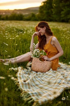 happy redhead woman sits in a field of daisies on a plaid during sunset and enjoys nature. High quality photo