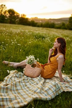 happy redhead woman sits in a field of daisies on a plaid during sunset and enjoys nature. High quality photo