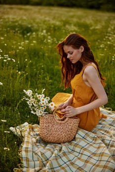 happy redhead woman sits in a field of daisies on a plaid during sunset and enjoys nature. High quality photo