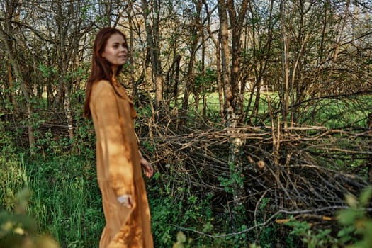 a beautiful, slender woman with long hair walks in the shade near the trees, dressed in a long orange dress, enjoying the weather and the weekend. High quality photo