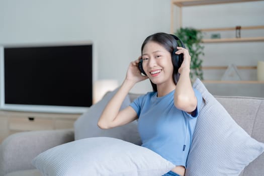 Peaceful girl in modern wireless headphones sit relax on comfortable couch listening to music, on cozy sofa, stress free concept