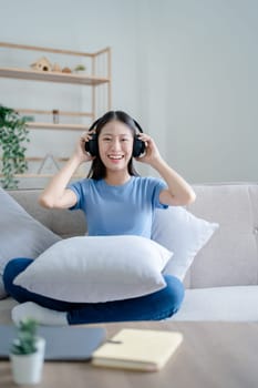 Peaceful girl in modern wireless headphones sit relax on comfortable couch listening to music, on cozy sofa, stress free concept