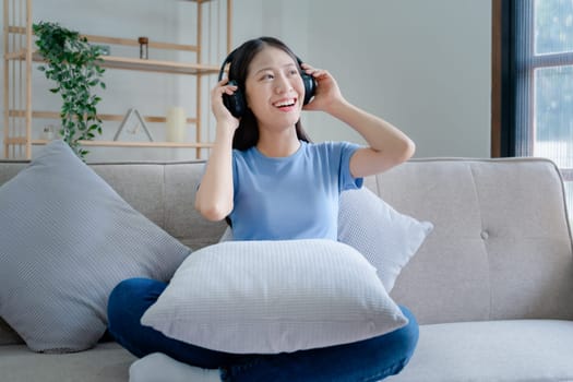 Peaceful girl in modern wireless headphones sit relax on comfortable couch listening to music, on cozy sofa, stress free concept