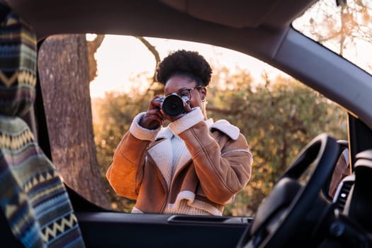 young african woman taking photos with a camera during a road trip in camper van, concept of van life and travel adventures