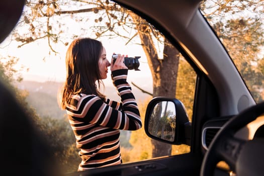 young caucasian woman taking photos of nature with a camera during a road trip in camper van, concept of van life and travel adventures