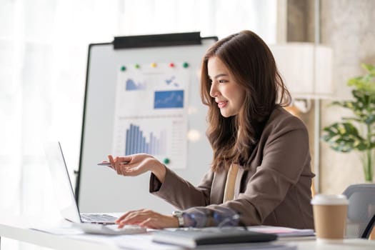 Cheerful business lady working on laptop in office, Asian happy beautiful businesswoman in formal suit work in workplace. Attractive female employee office worker smile...